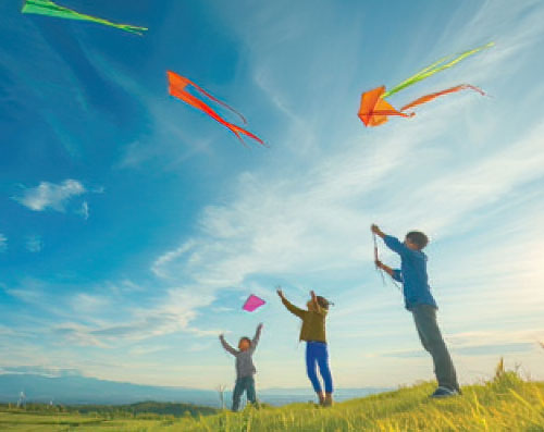 Image of kids playing with kites on an open field with hills in the background