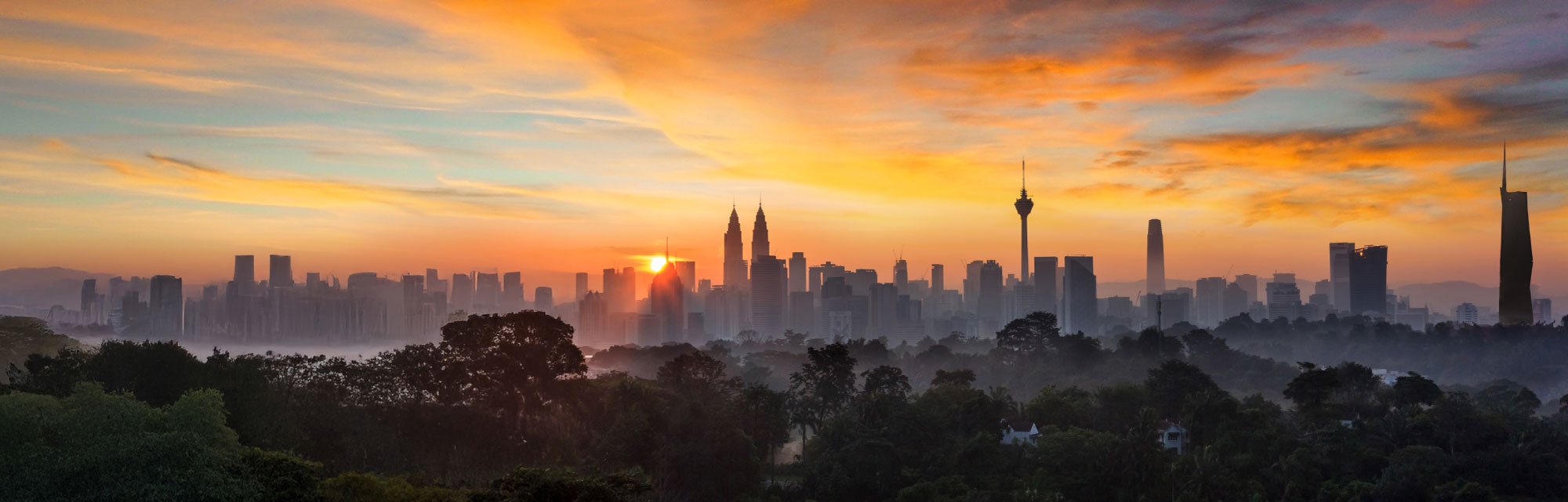 Majestic panoramic view of KL city skyline set against a setting sun.