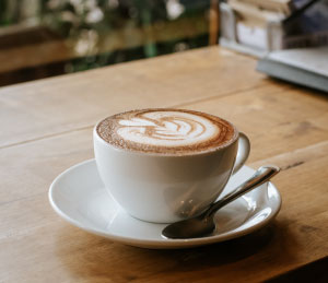Hot cappuccino with latte art served in a white cup on a wooden table in a cozy café