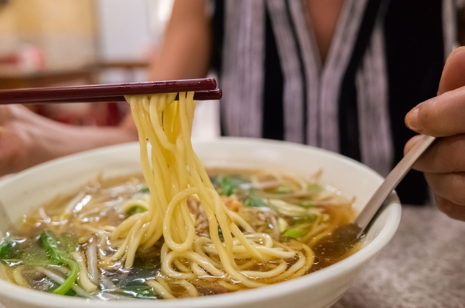 Close-up of a bowl of noodles being lifted with chopsticks