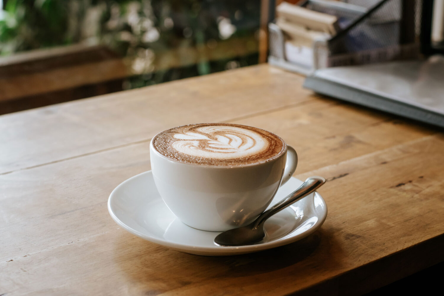 Hot cappuccino with latte art served in a white cup on a wooden table in a cozy café